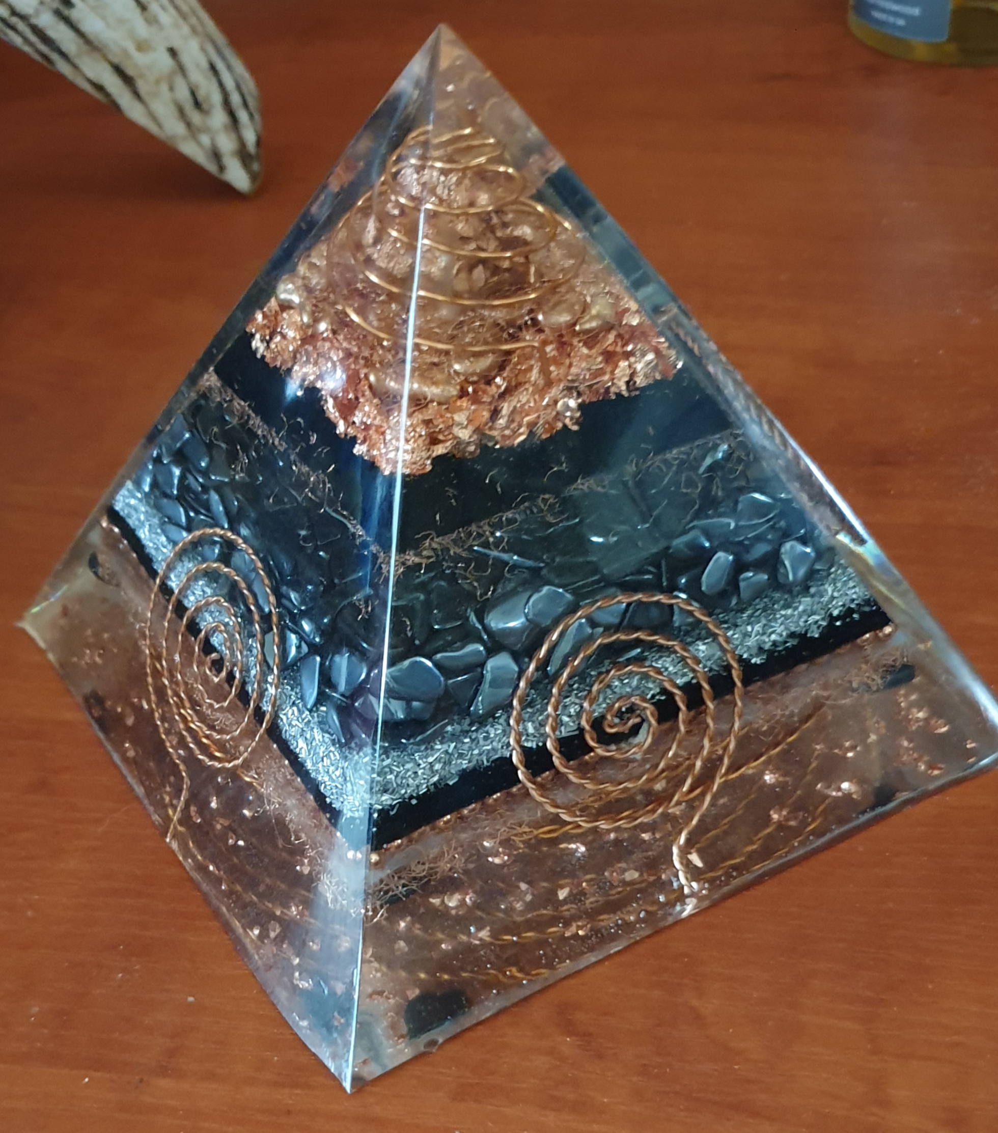 Earth-toned orgonite pyramid with dark stone layers and copper coil