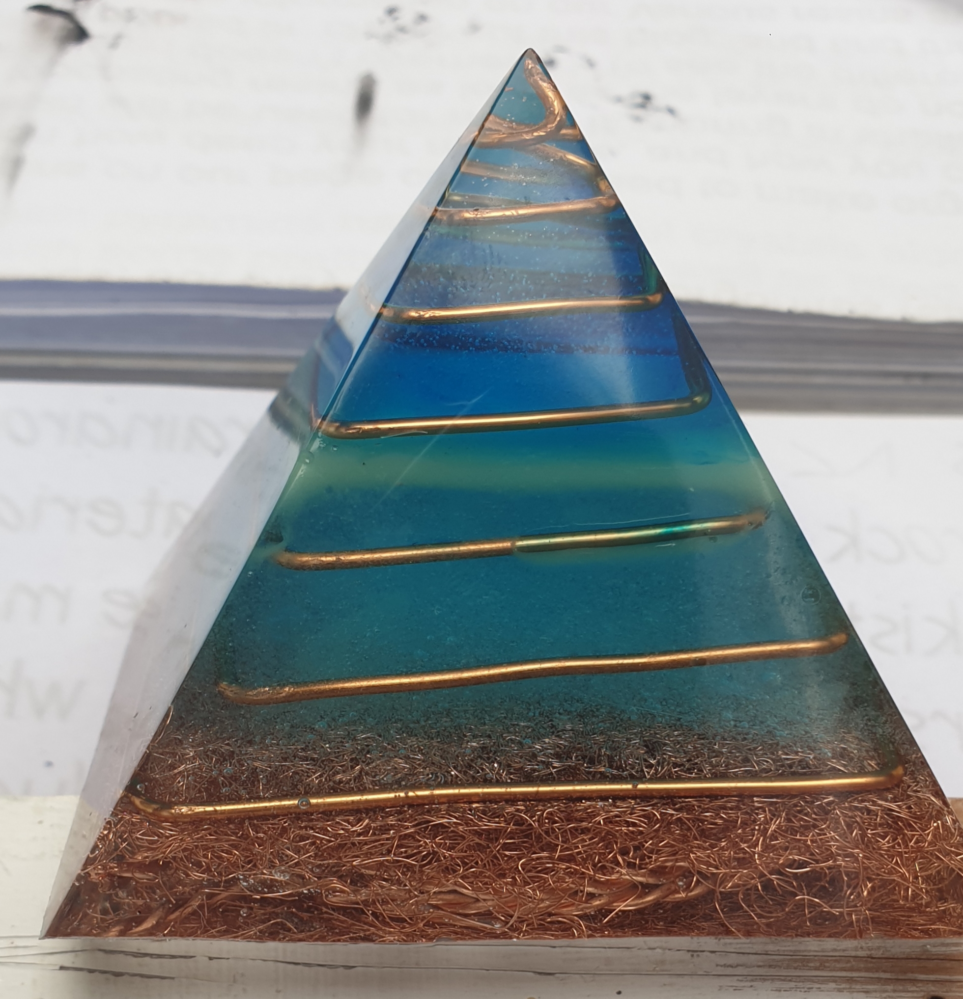 Turquoise and copper orgonite pyramid catching natural window light on the Cape Peninsula